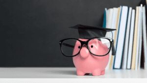 piggy bank wearing graduation cap and glasses with books in background