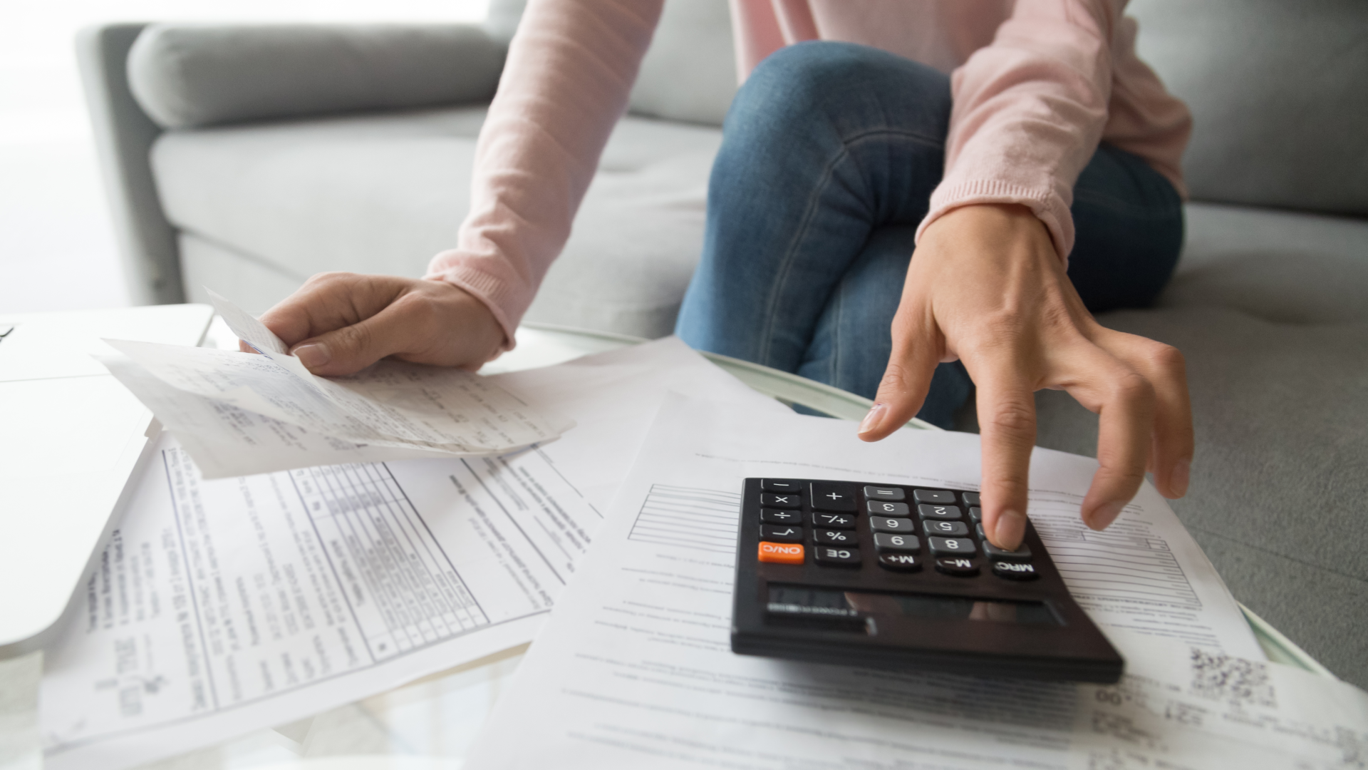 a woman types on a calculator while reviewing paperwork on her coffee table