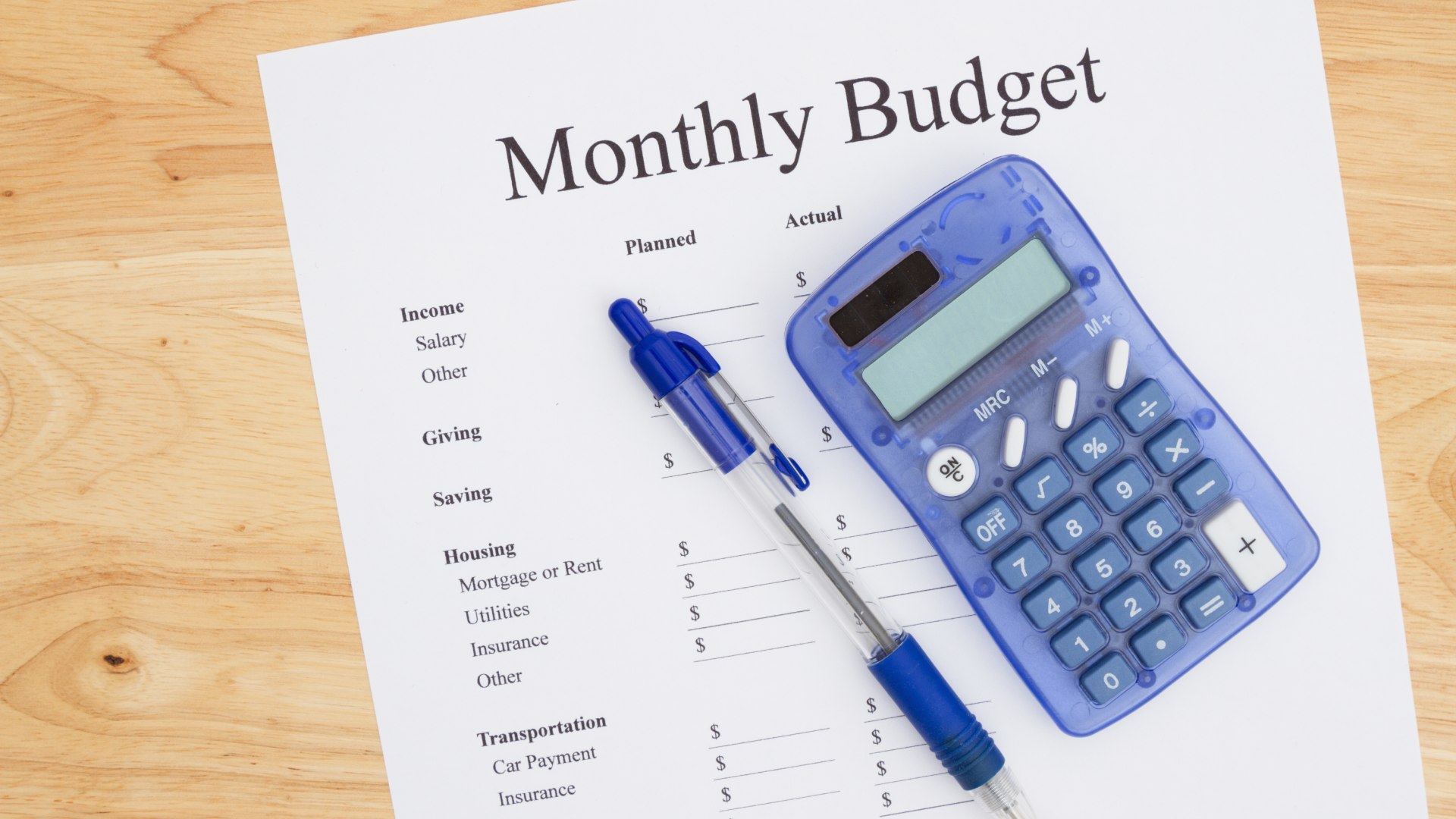 a paper listing the monthly budget with a pen and calculator sitting on top