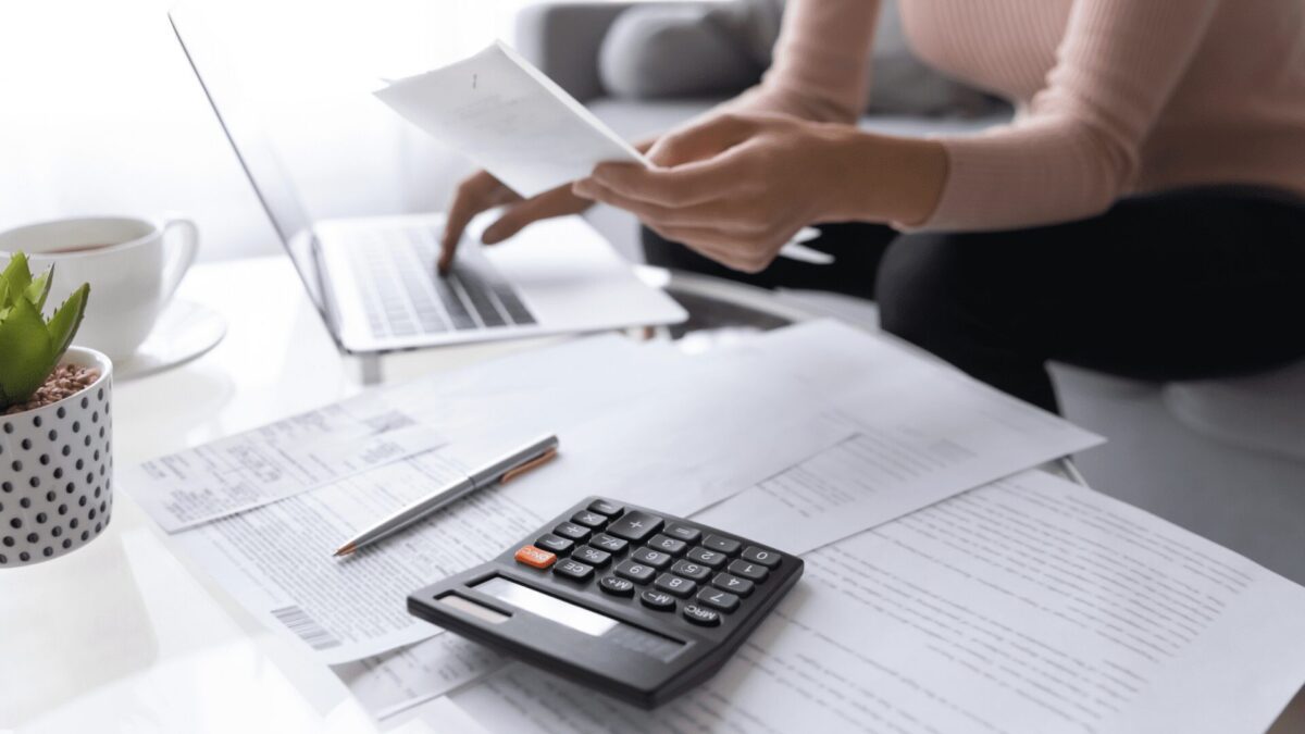 a woman calculates loan payments with calculator, paperwork and laptop