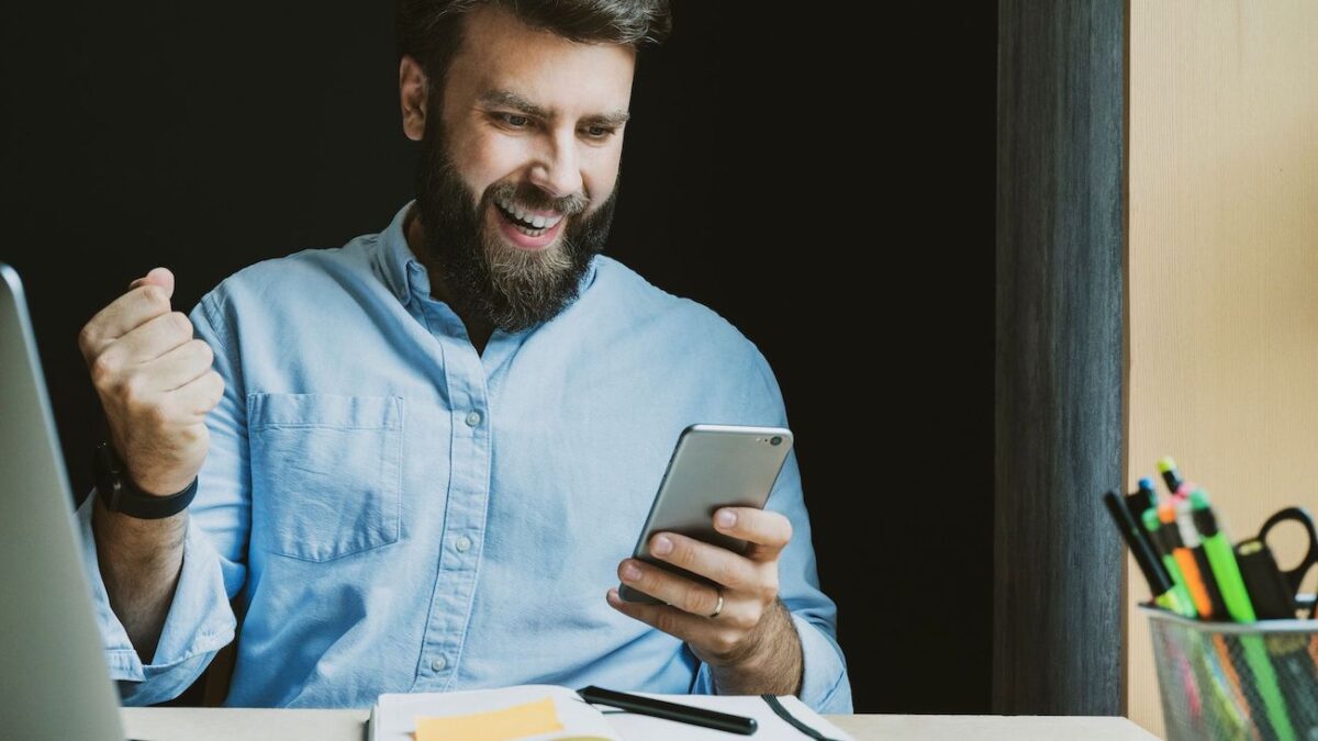 Bearded man smiling and cheering while looking at his phone | Wise Loan