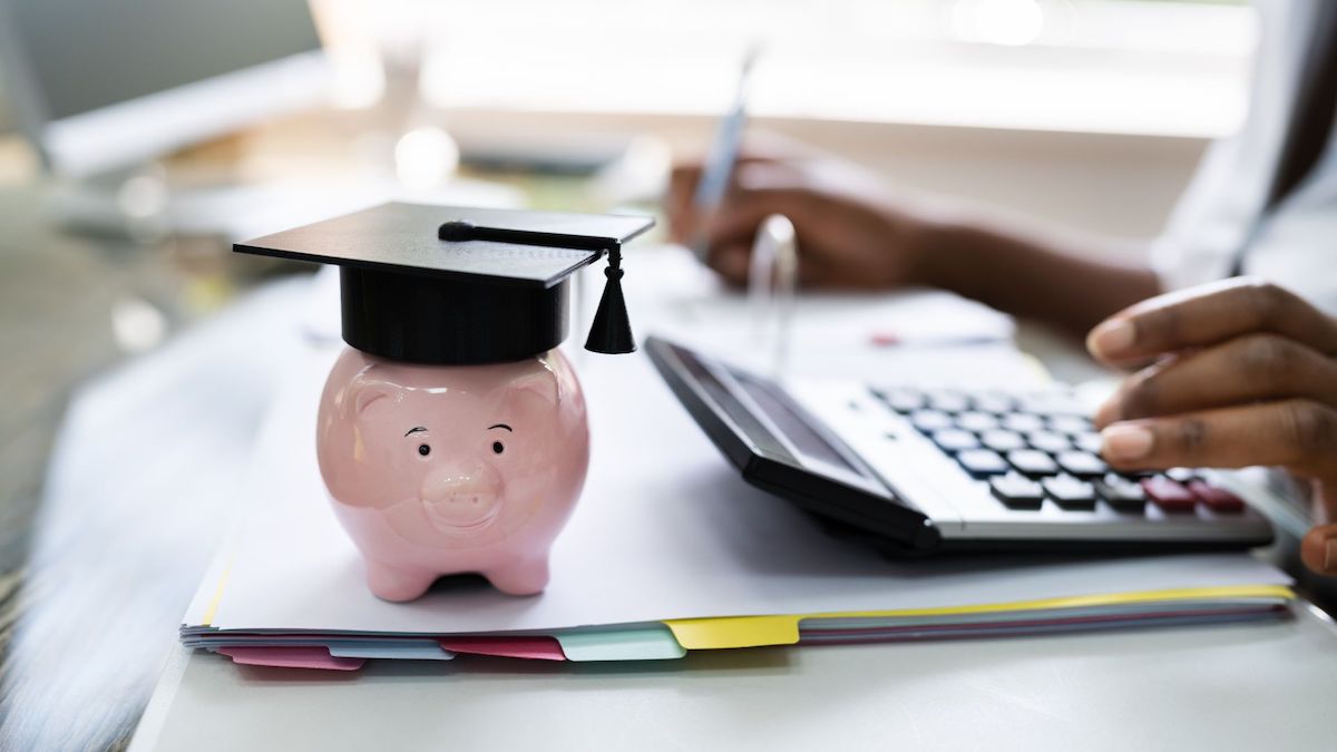 Ceramic piggy bank wearing a graduation cap on person's desk while they calculate loan payment | Wise Loan