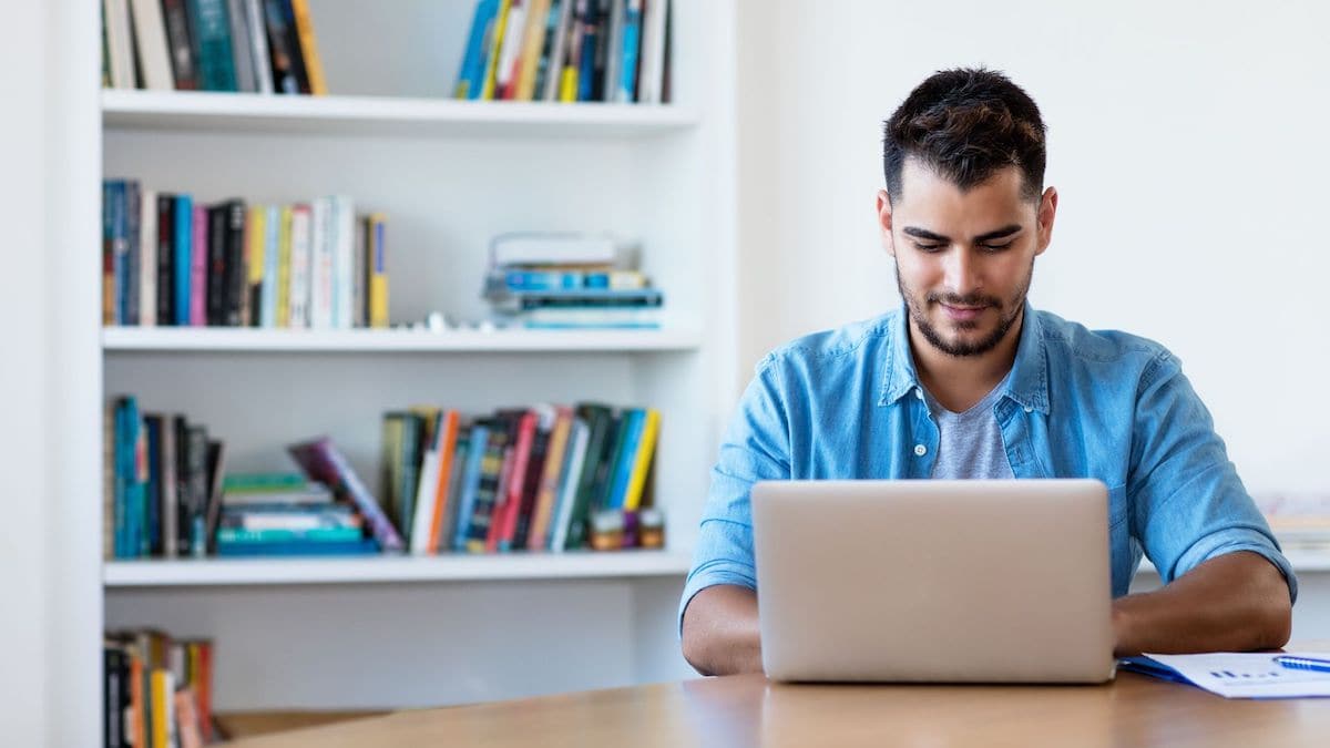 Man smiling while working on laptop in library | Wise Loan