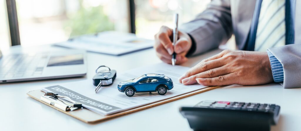 Keys and toy car sit on desk as auto dealer finishes writing contract | Auto repair financing options
