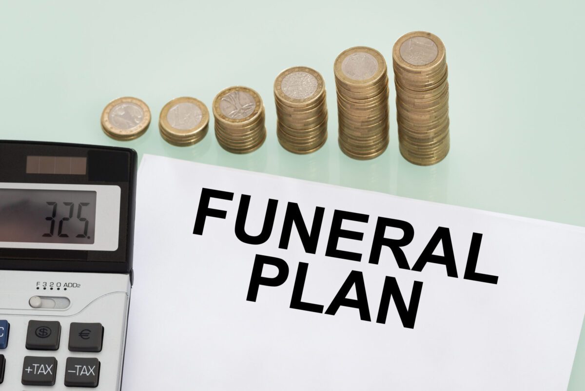 Paper marked as funeral plans rests next to stack of coins and calculator | Funeral financing options