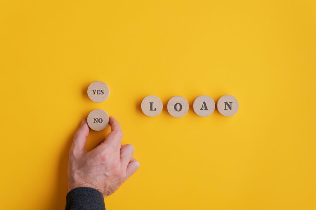 Person places wooden block on yellow background to spell the word, “Loan” | Home repair financing