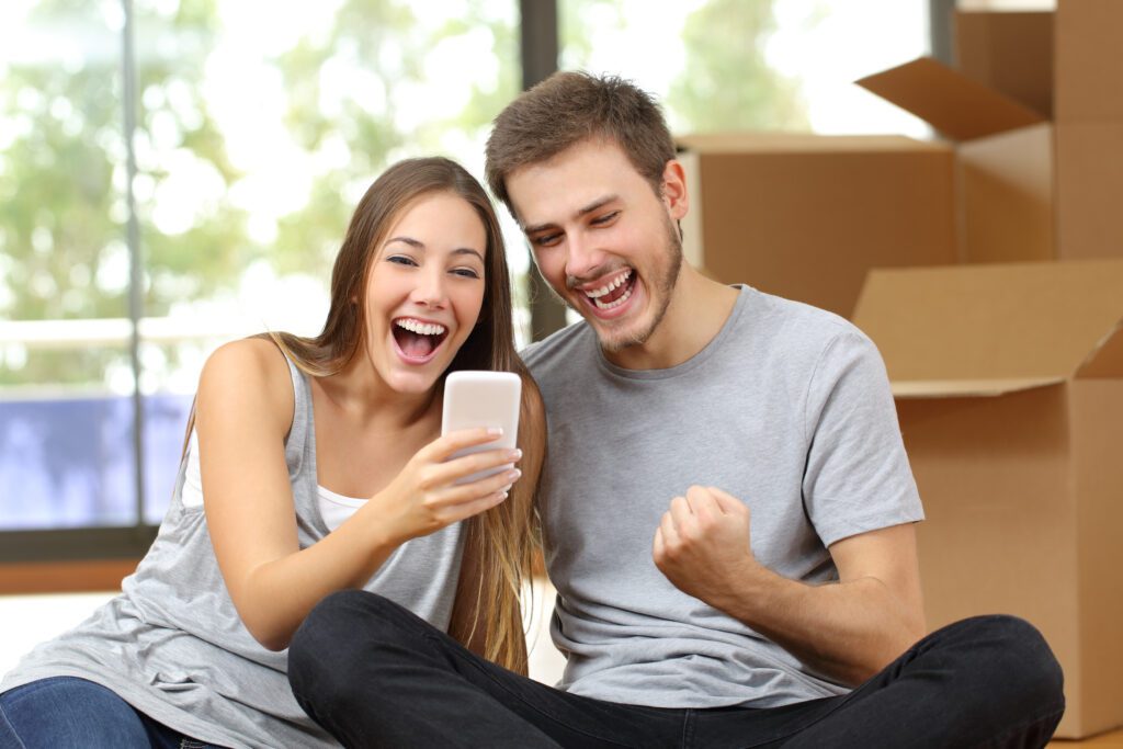 Happy couple cheers while sitting on couch and applying for Wise Loan | Relocation financing options