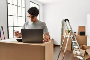 Man uses laptop as it rests on cardboard boxes in an empty room | Relocation financing options
