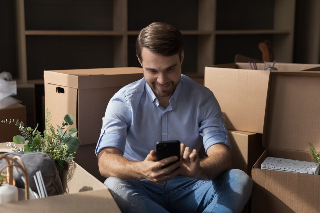 Man sitting with boxes smiles at phone while reviewing loan terms | Relocation financing options