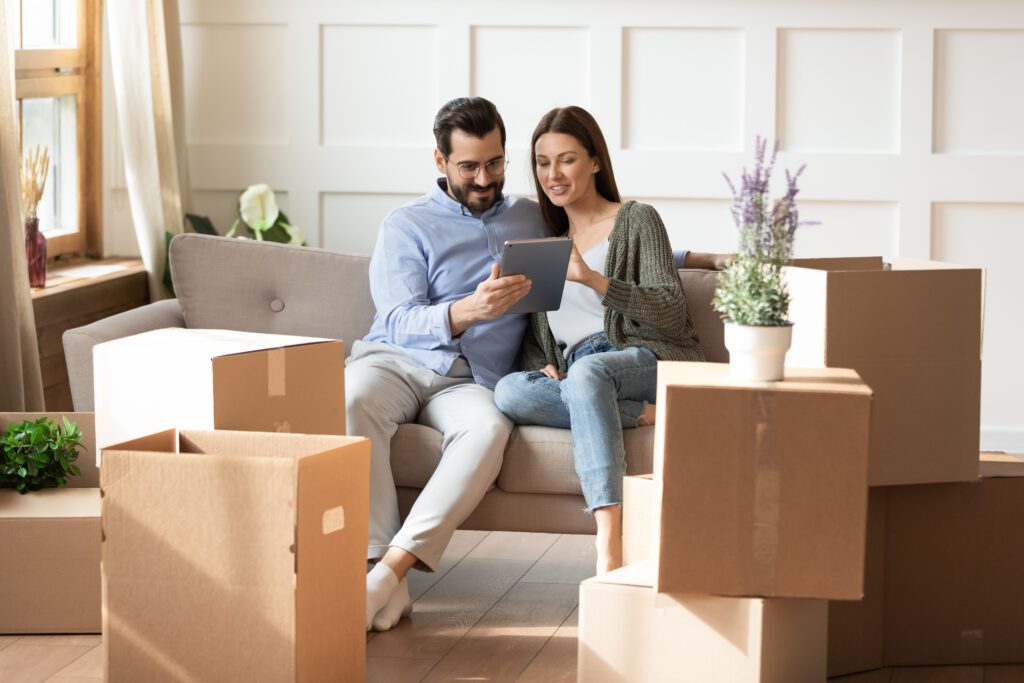Couple uses tablet to fill out relocation loan form amongst packed boxes | Relocation financing options