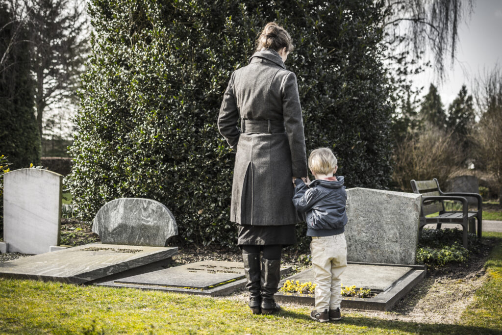 Woman holds hand of little boy as they stand in front of headstone in cemetery | How to get a funeral loan