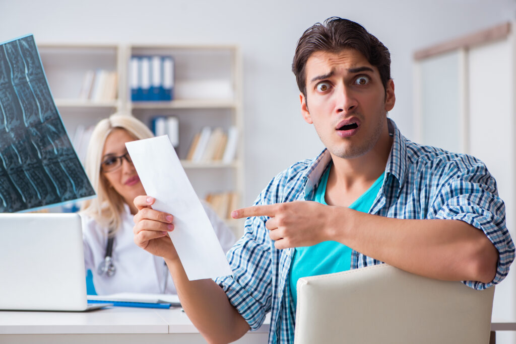 Shocked man with jaw dropped points to white paper while sitting in medical office | How to get a medical loan