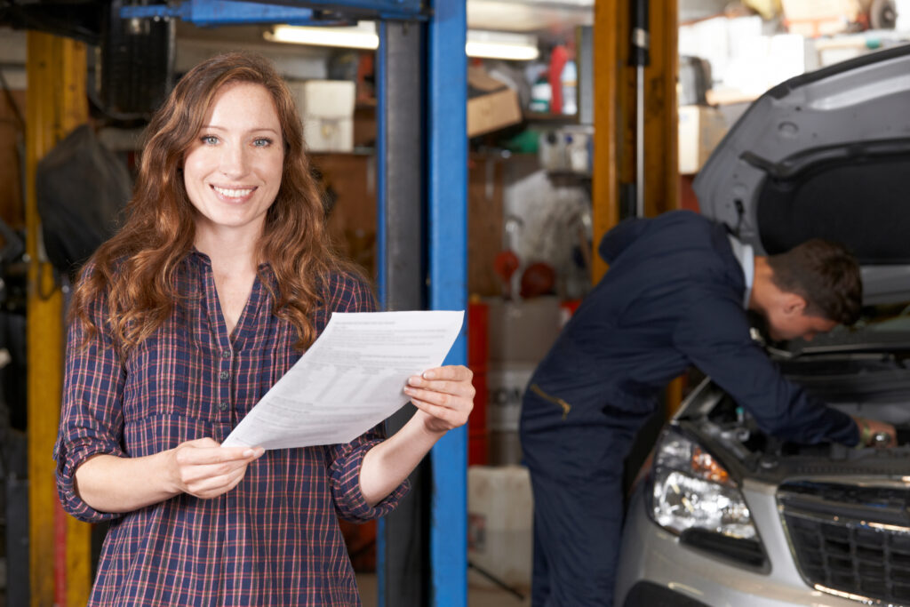 Woman in plaid smiles while holding auto repair bill knowing she has loan to cover expenses | How to get an auto repair loan