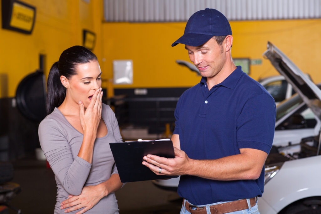 Shocked woman puts hand over mouth as mechanic shows her clipboard of repair costs | How to get an auto repair loan
