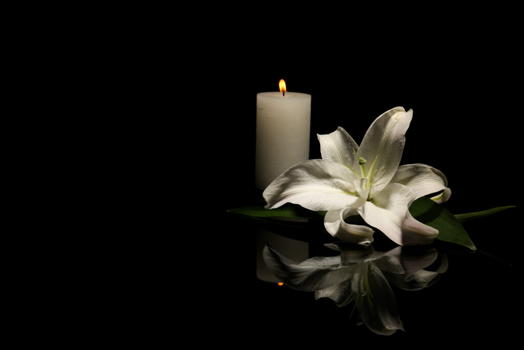 White lily and lit memorial candle sit on black background | How to get a funeral loan