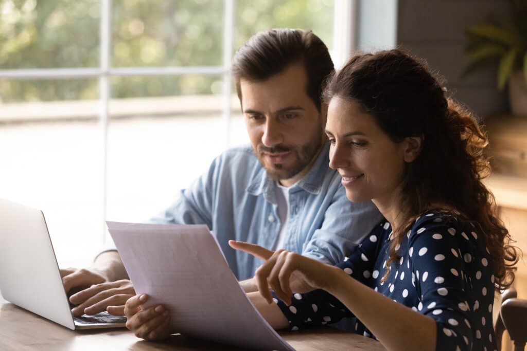 Happy couple smiles as they compare installment loans on laptop and printed paper | Best installment loans