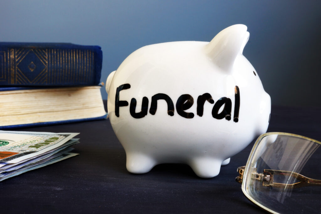 Piggy bank labeled as funeral sits on black desk with books and eyeglasses | How to get a funeral loan