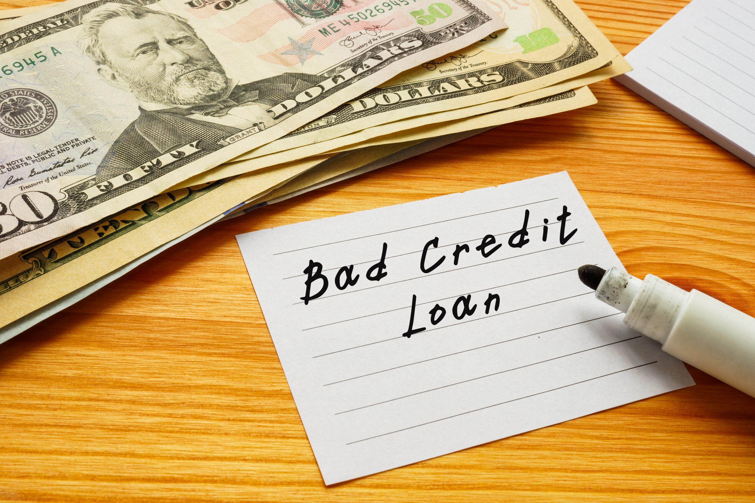 Sticky note labeled as bad credit loan rests next to stack of cash | Best emergency loans for bad credit