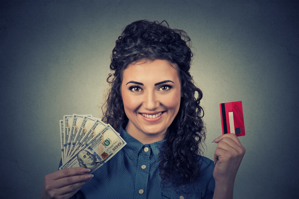 Smiling woman holds hundred-dollar bills in one hand and credit card in other | Ways to get emergency money