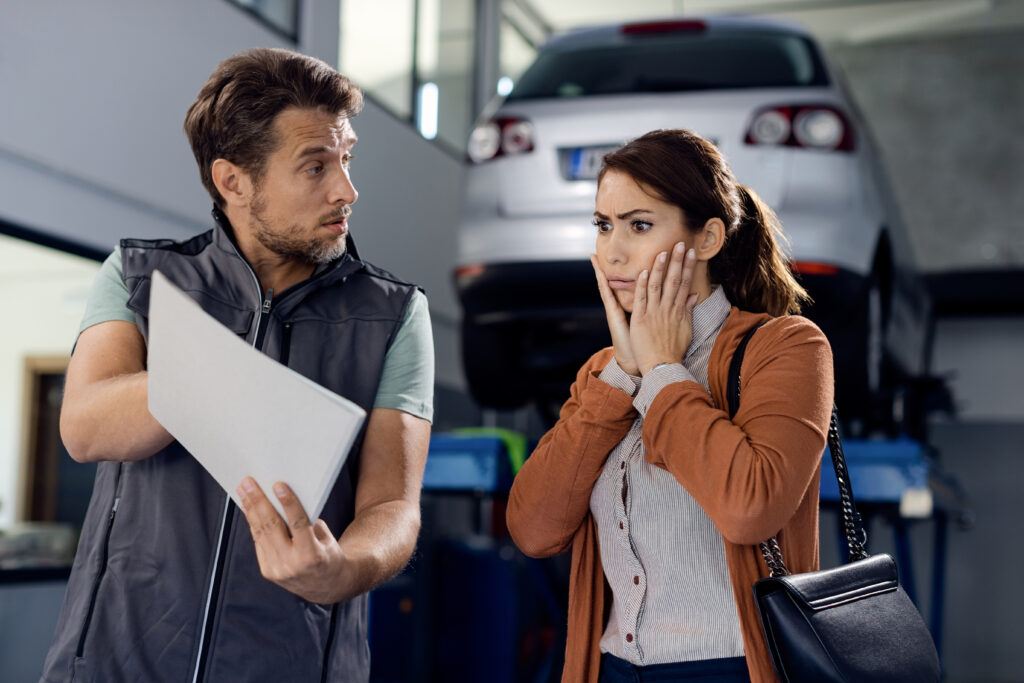 Shocked woman puts hands on cheeks as mechanic shows her printed car repair expenses | How to get an auto repair loan