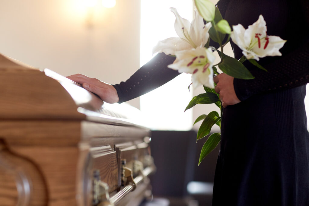 Person in suit holds white lilies as they place hand on wooden casket | How to get a funeral loan