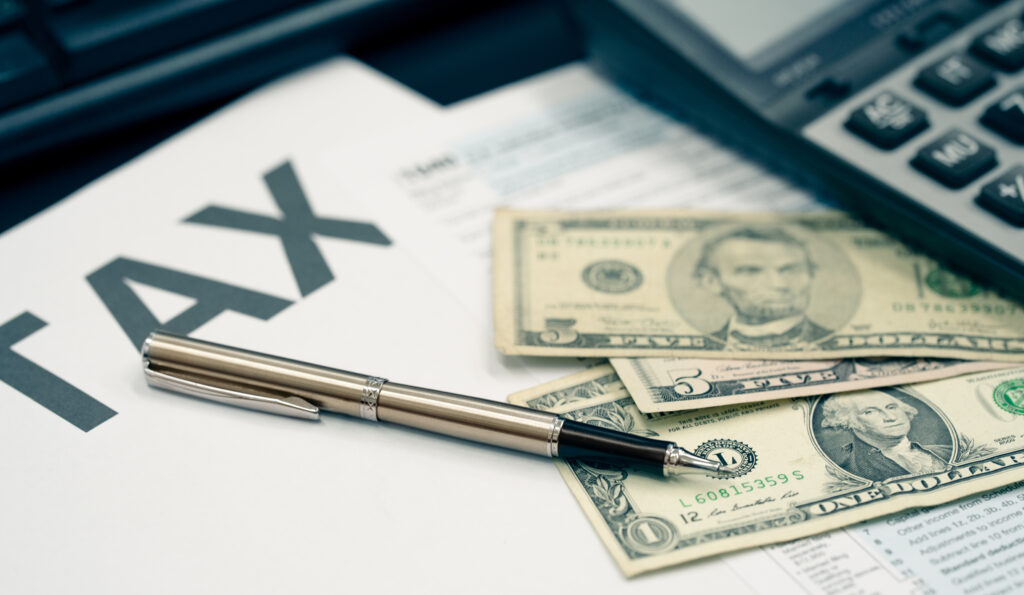 About tax documents with a pen, calculator, and American currency, including one dollar bill and $ 5