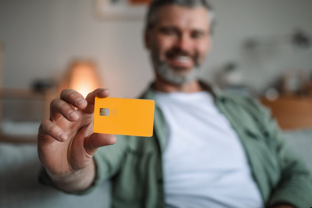 A smiling man sitting inside carrying a yellow card without contact towards the camera