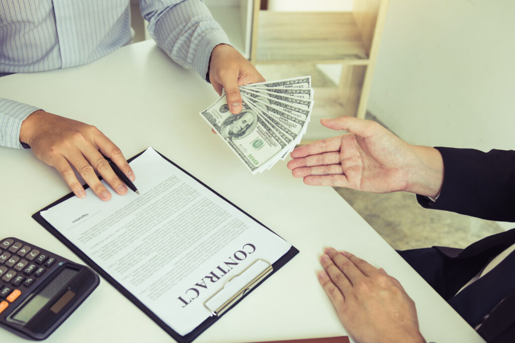 Two hands exchanging cash above a contract on a desk.