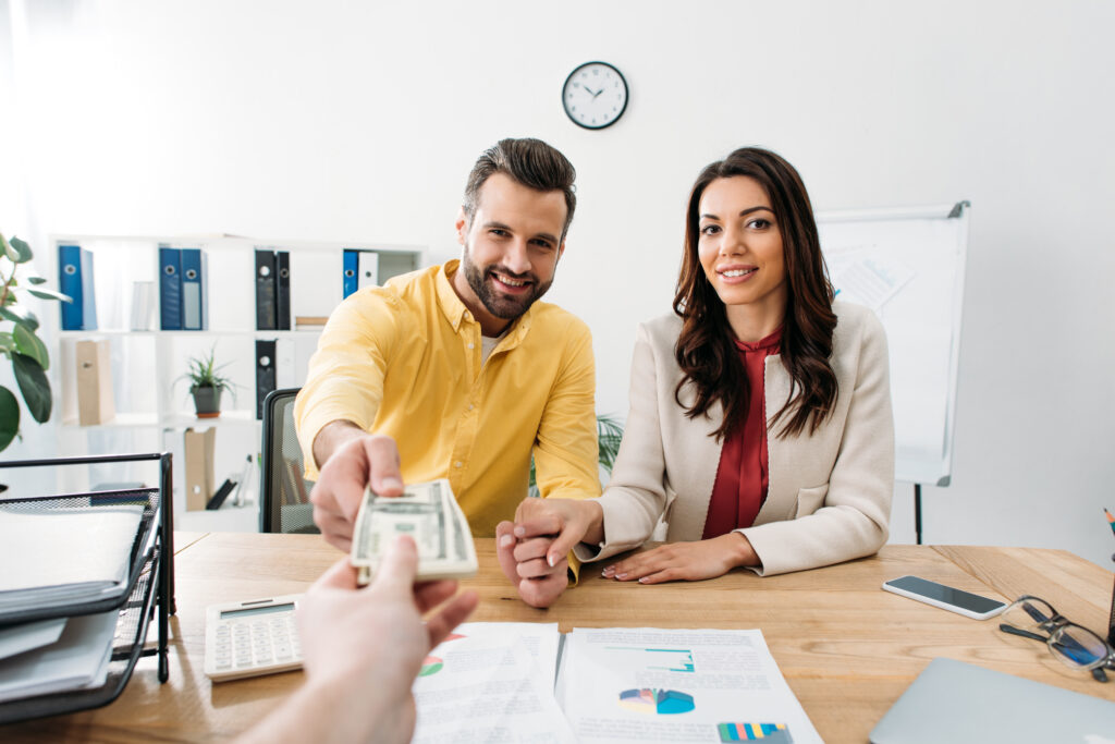 A smiling couple at a desk receives money, symbolizing a financial transaction